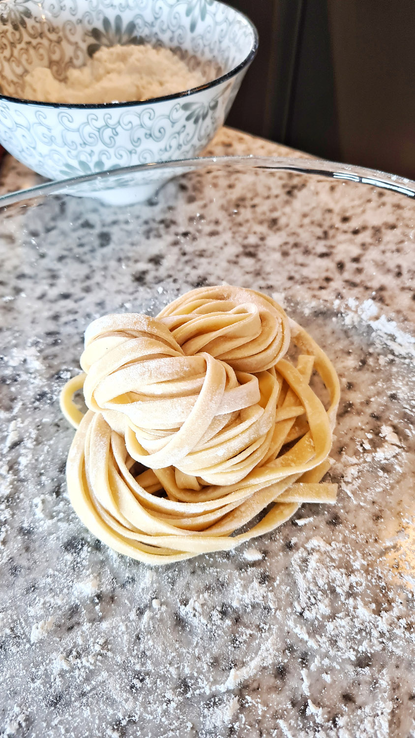 Fresh handmade fettuccine nest on a floured surface.