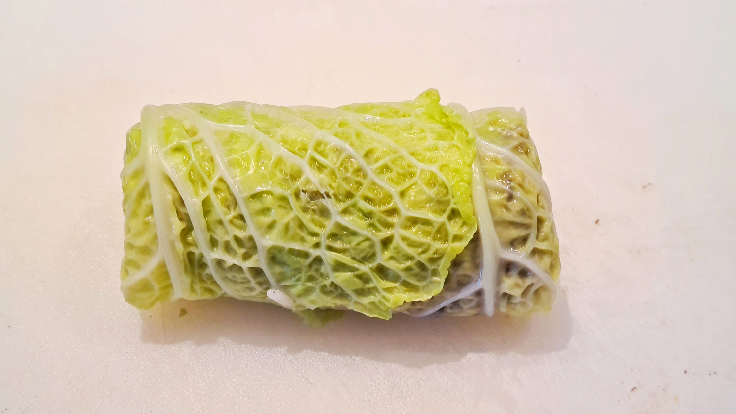 Hand-shaped stuffed savoy cabbage roll ready for braising