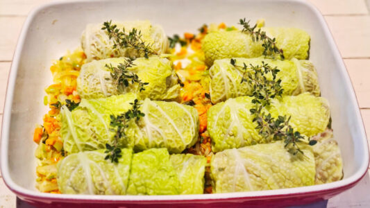 French stuffed cabbage rolls with thyme arranged over vegetables before braising