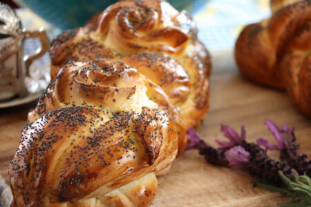 Braided challah loaves with poppy seeds resting on a wooden table, a cozy bakery scene in the background.